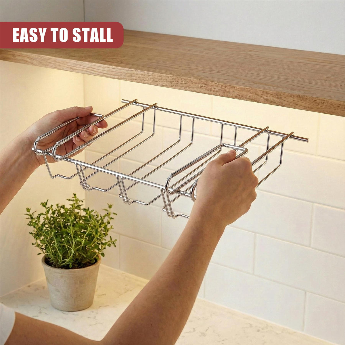 Hands holding a stainless steel under shelf wine glass rack beneath a wooden kitchen shelf next to a potted plant