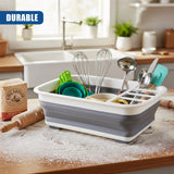 The collapsible dish drainer holds whisks, scoops, and various kitchen utensils on a flour-dusted counter.