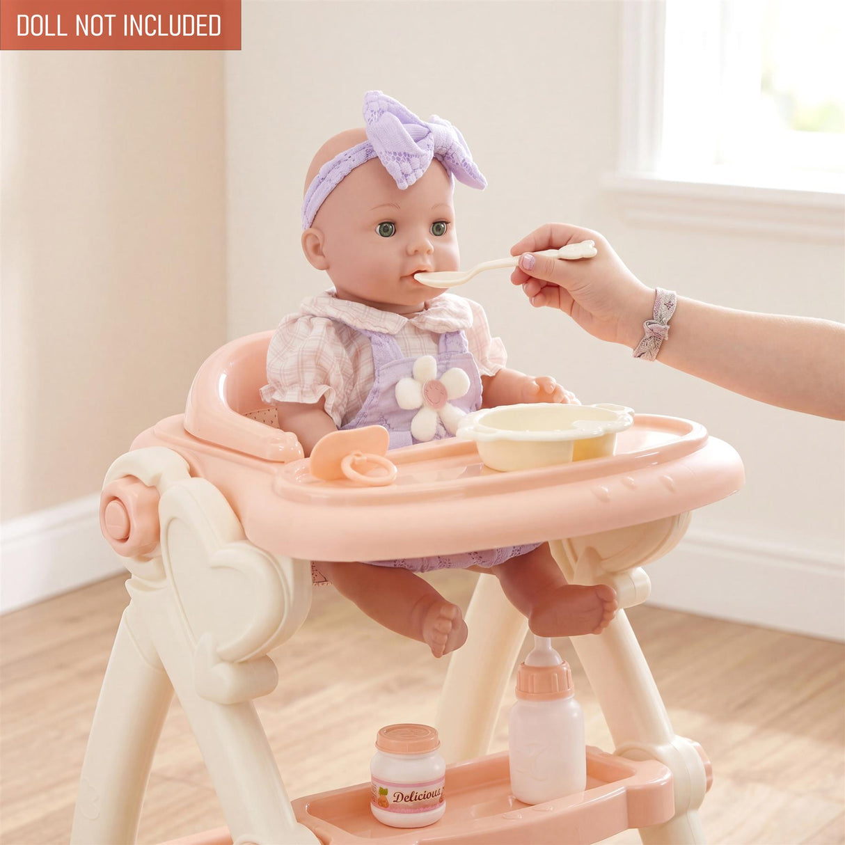 A doll sits in a high chair while a hand feeds it with a spoon and accessories.