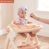 A doll sits in a high chair while a hand feeds it with a spoon and accessories.