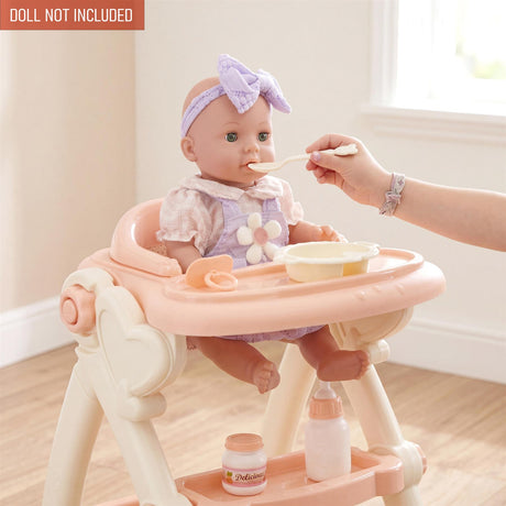 A doll sits in a high chair while a hand feeds it with a spoon and accessories.