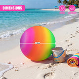 A large, gradient-colored spherical item sits on beach sand with a pail and rolled towel.