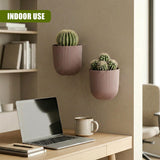 Set of two ribbed pink planters holding small artificial succulents mounted on a neutral wall.