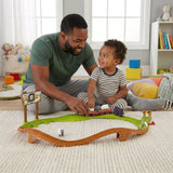 Father and son play with a green and brown train track set and toy pieces on a carpeted floor.