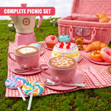 A collection of pink teacups, desserts, pastries, and a checkered picnic basket are displayed.