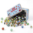 An open tin box is filled with a large collection of assorted colored glass marbles on a white surface.