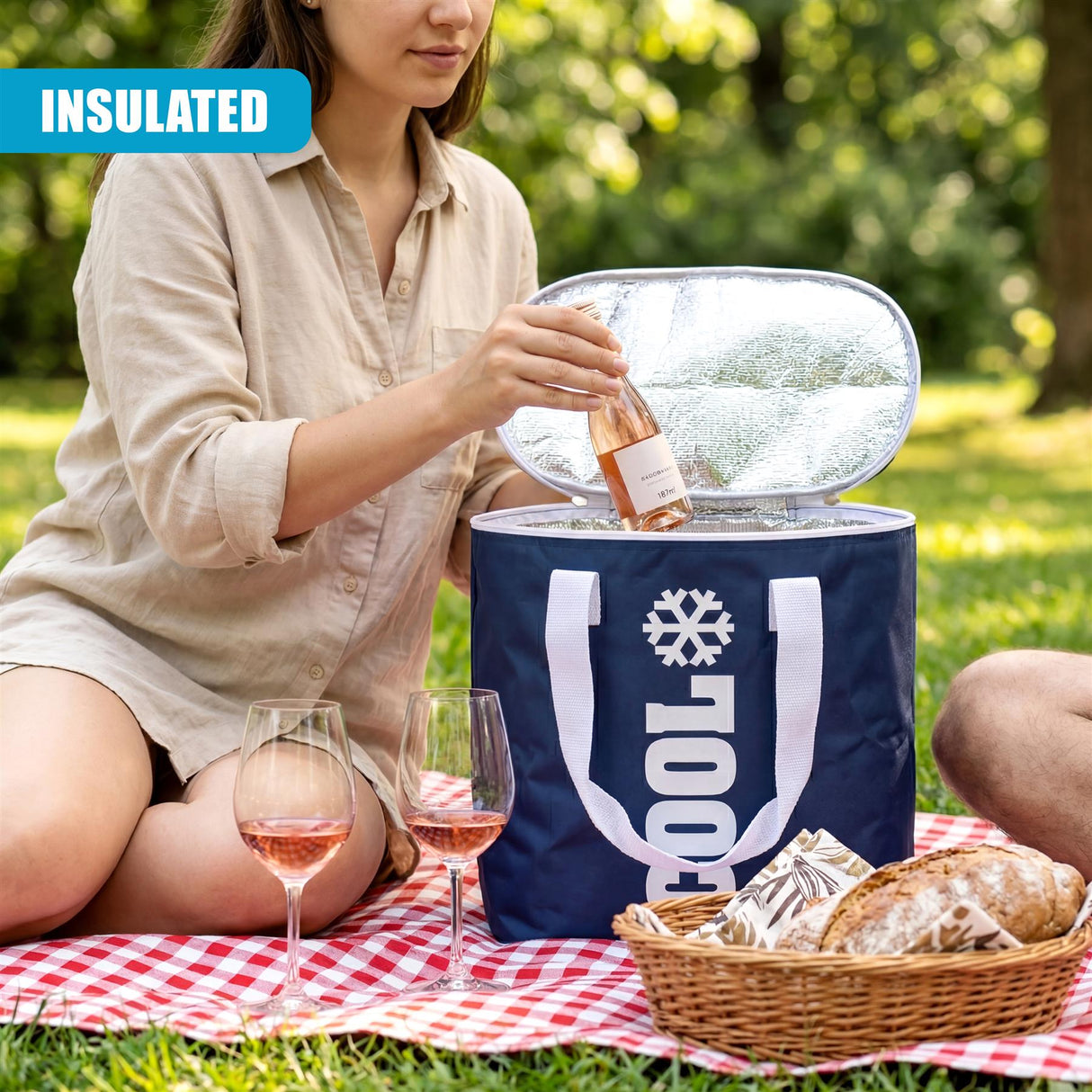 Woman opening a blue cooler bag on a blanket, placing wine bottles near bread and wine glasses.