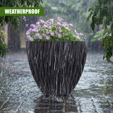 Large black planters filled with purple flowers sit on wet stones during heavy rainfall.