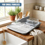 Gray dish drying rack on a wooden counter filled with clear glassware and assorted utensils.