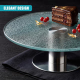 Transparent glass turntable stand with metal base, holding a slice of cake and red cherries.