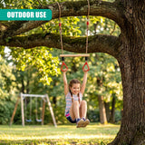 A young girl smiles while swinging from a trapeze bar attached to a large, horizontal tree branch.