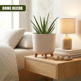 Beige planter pot with small wooden legs holds a tall green succulent on light wood furniture.