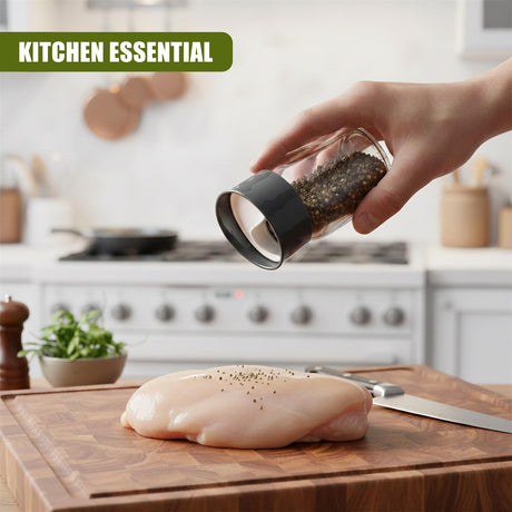 Hand holding a glass cruet sprinkles spices over raw chicken on a wooden cutting board.