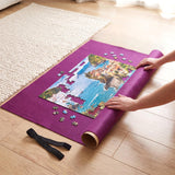 Hands place puzzle pieces onto a purple mat featuring a sunny coastal scene.