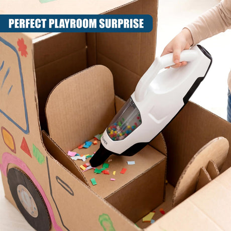 A white toy vacuum cleaner rests inside an open, decorated cardboard box with scattered colorful pieces.