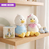 Two plush Easter chicks and small knitted booties sit next to a seasonal decorative item on a shelf.