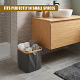 A gray fabric laundry hamper sits on the floor, holding folded towels and clothes next to a wood vanity.