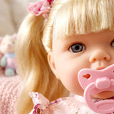 Close-up of the doll's face showing blonde hair, blue eyes, and a pink pacifier.