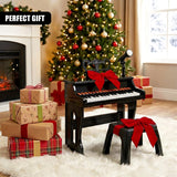 A child's black electronic keyboard with red bow on top of presents in front of a decorated Christmas tree. - UKBuyZone