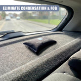 A small, black packet dehumidifier sits on the car's dashboard, viewed through the windshield.