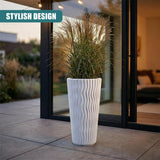 Vertical white planter with ribbed sides holds a large arrangement of feathery ornamental grasses.