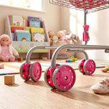 Pink caster wheels attached to a metal frame support a kids doll shopping trolley.