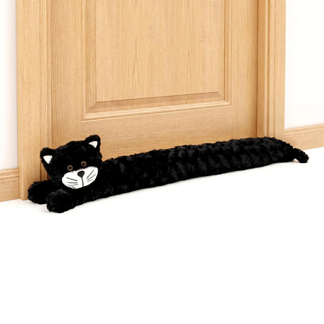 Black cat-shaped fabric draught excluder lying along the base of a light wooden door.