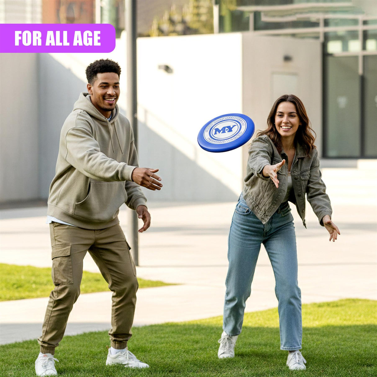 Man and woman smiling on green grass near buildings, tossing a blue frisbee.