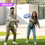 Man and woman smiling on green grass near buildings, tossing a blue frisbee.