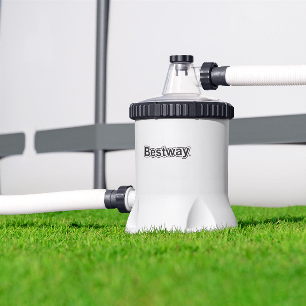 White Bestway pool filter pump sits on green grass with connected white pipes.