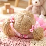 Blonde doll with hair styled in pigtails rests on a textured pink blanket near a bear.