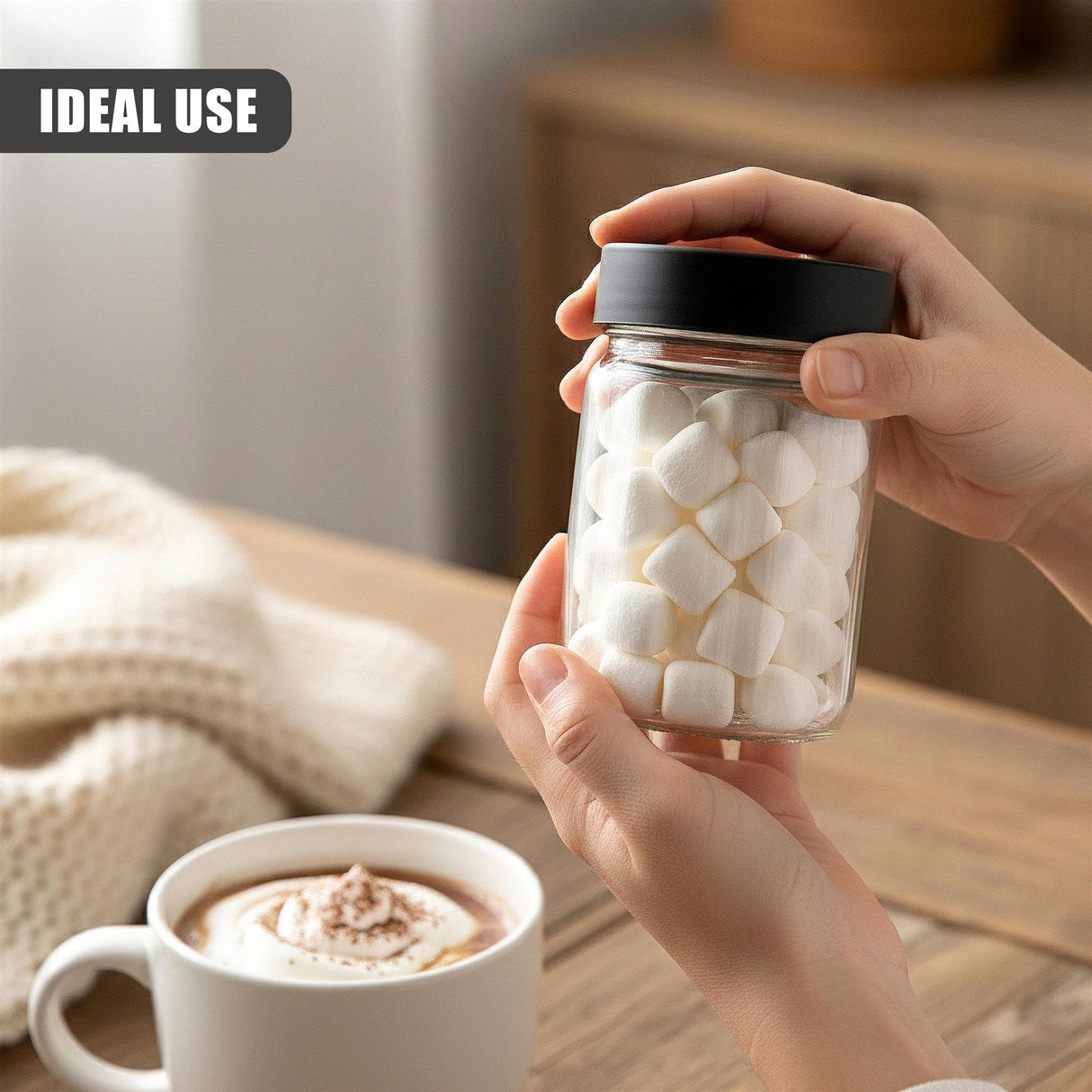 A hand holds a clear glass jar of white cubes next to a white mug containing a beverage.