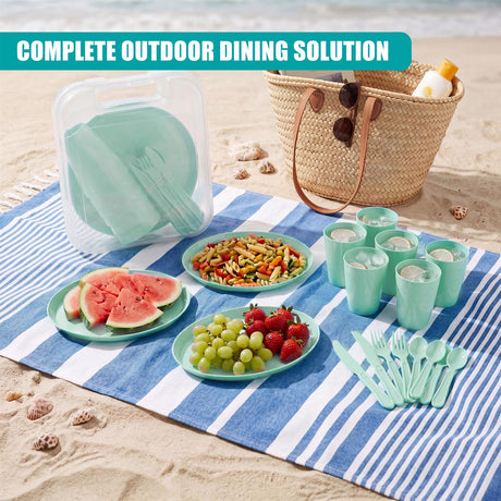 Picnic items, including tableware, snacks, fruit, and utensils, are arranged on a blue striped blanket.