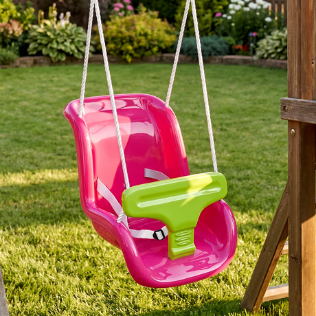 A pink toddler swing seat with a green safety bar and white straps hanging from ropes against a grassy garden background