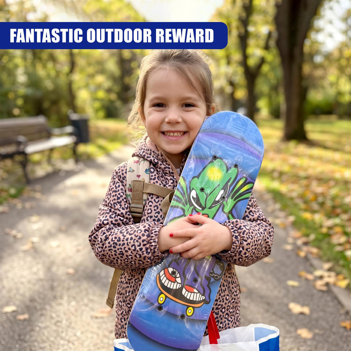 A smiling girl holds a colorful skateboard designed with green, blue, and black cartoon characters.
