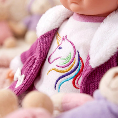 Doll wears a purple jacket with a white collar and a cream shirt displaying an embroidered unicorn.