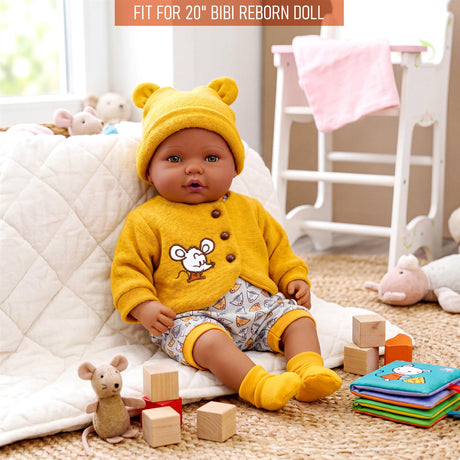 A doll wears a mustard yellow mouse outfit, shorts, beanie, and matching booties.