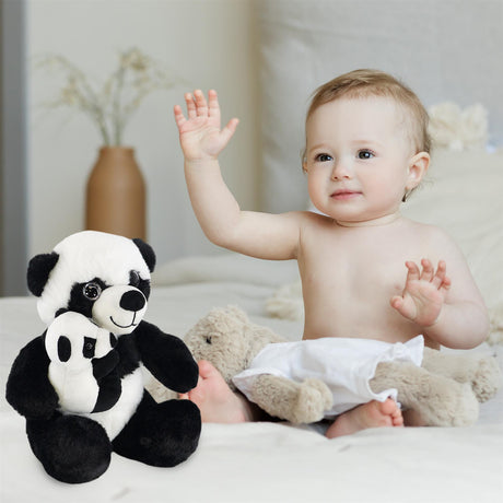 A happy baby sitting on a bed, waving one hand, next to a plush panda toy hugging a smaller panda. The baby is dressed in a diaper and has fluffy hair, while another soft toy in the background resembles a teddy bear. This image showcases a cozy and playful scene ideal for highlighting the Magic Toy Shop Super Soft Mommy & Baby Panda Plush Toy, perfect for young children. ukbuyzone.