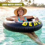 Smiling woman sitting in a large black inflatable tube floating in clear ocean water near a beach.