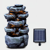 Tiered, dark gray rock waterfall structure with visible flowing water and an attached solar panel.