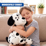 A young girl smiles while hugging a plush Dalmatian stuffed toy on a sofa.