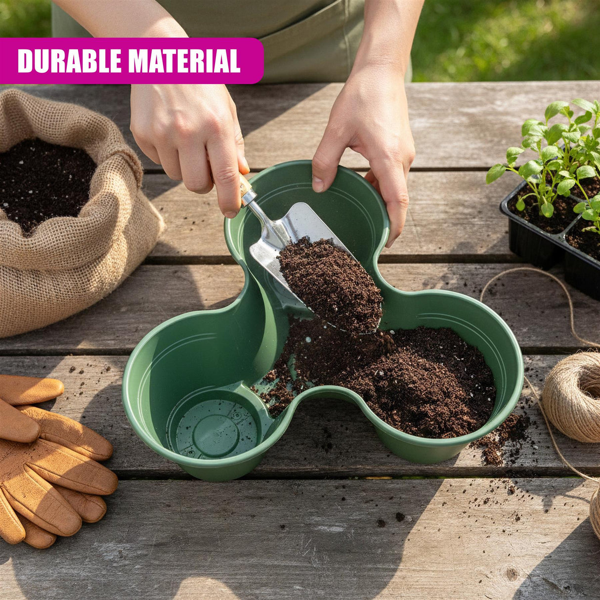 A pair of hands fills a green, curved planter with potting soil on a wooden surface.