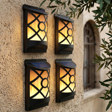 Four lit outdoor wall sconces with patterned panels mounted on a textured wall surface.