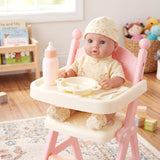 Doll sits in a pink high chair with a white tray, bottle, bowl, and washcloths accessory set.