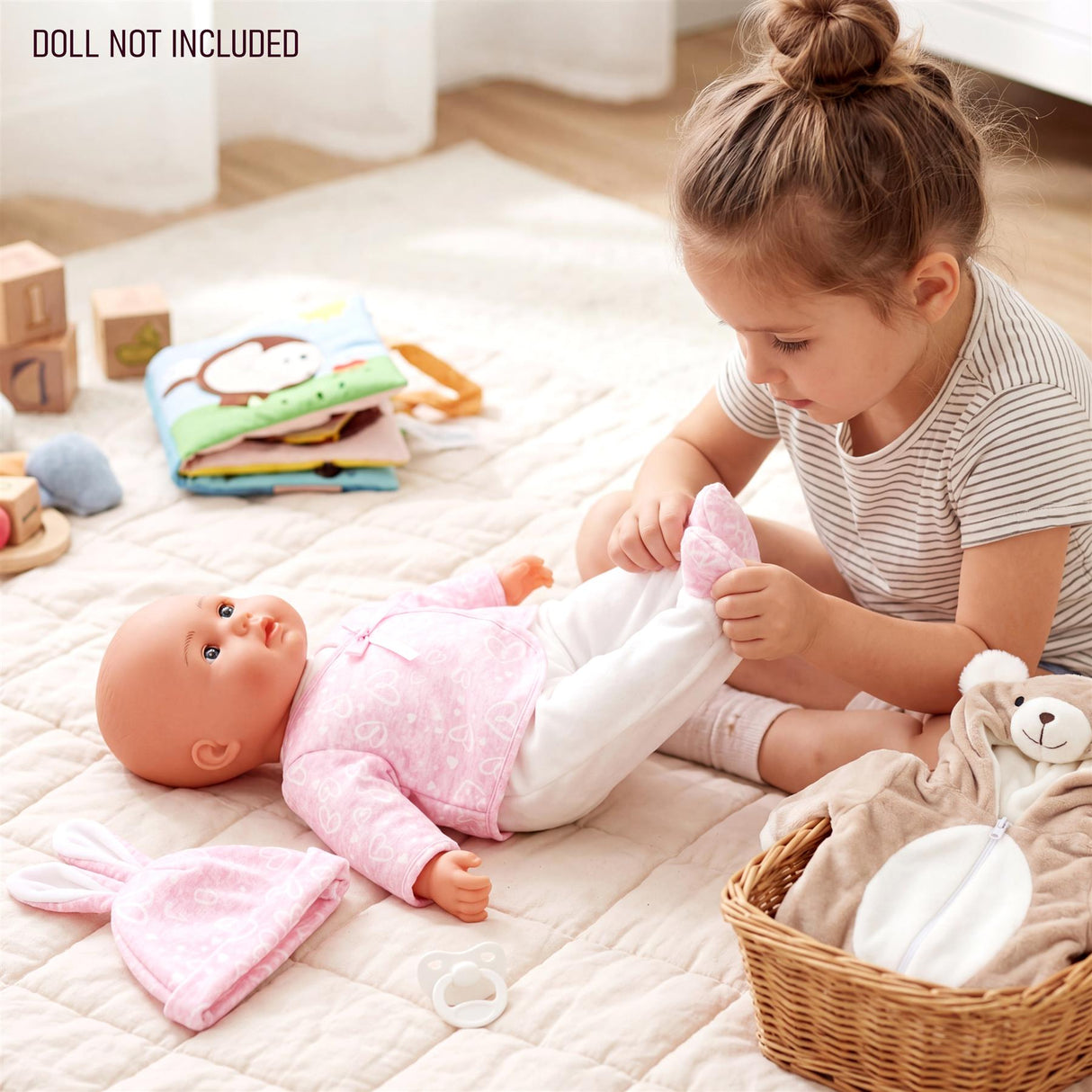 Doll lying on a rug, dressed in pink and white, next to bundled bear and bunny outfits.