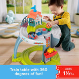 A toddler plays with a detailed train set featuring tracks and a miniature station house structure.