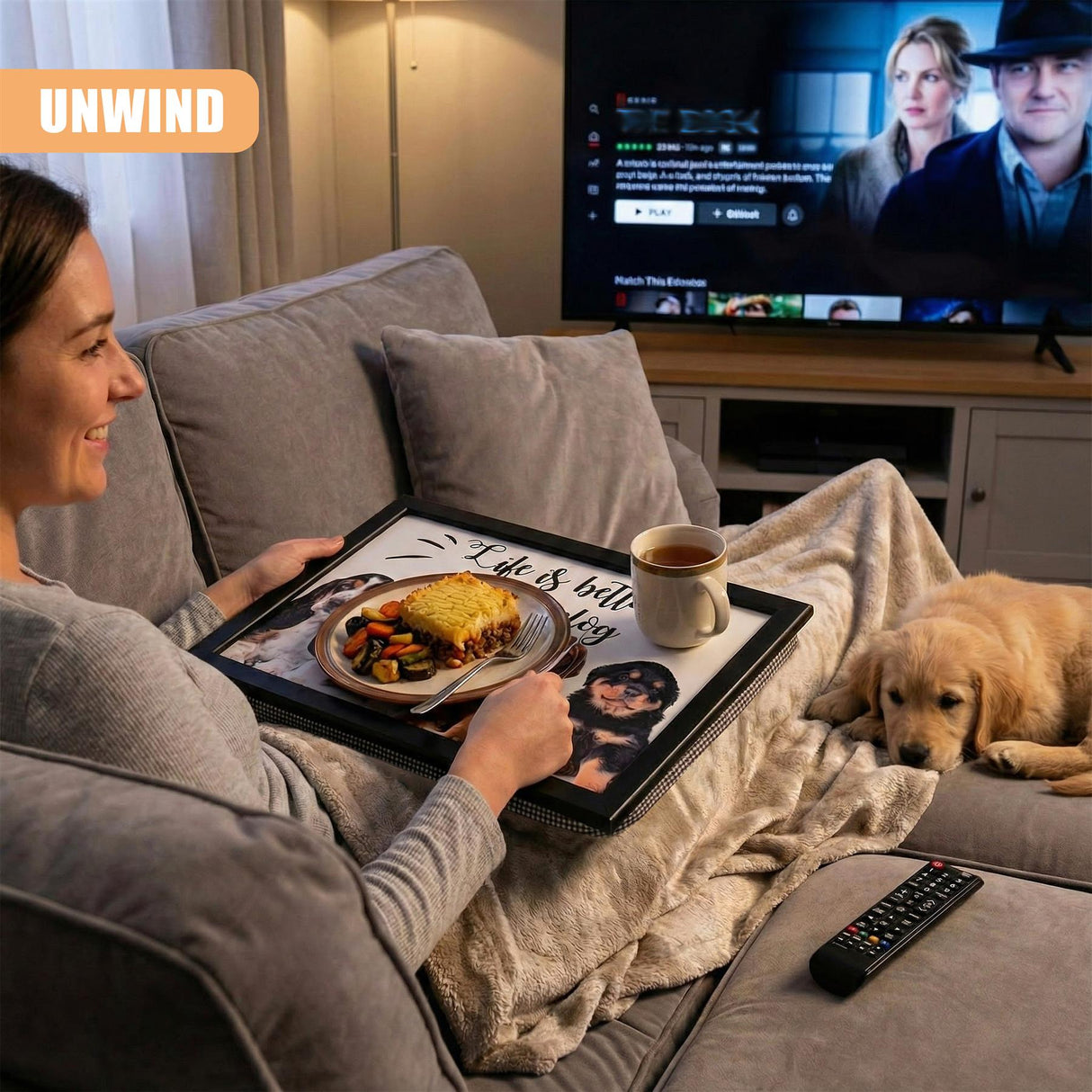 A woman sits on a couch, holding a tray with a plate of food, a cup of coffee, and a remote control. She's watching TV on a large screen in the background. The tray features a dog-themed design, and a dog is lying on the couch next to her. - UKBuyZone
