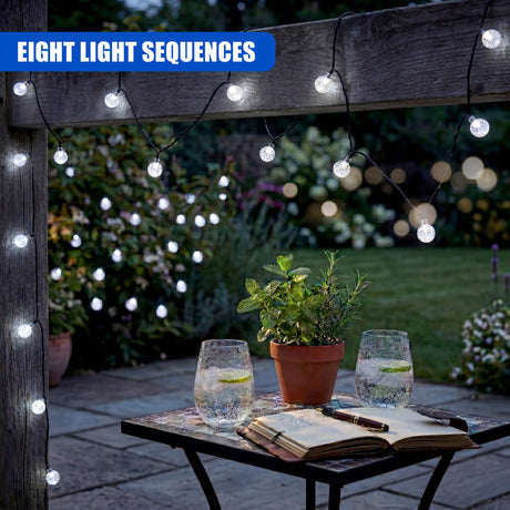 Decorative string lights hang from wood, illuminating a garden table with open books and glassware.