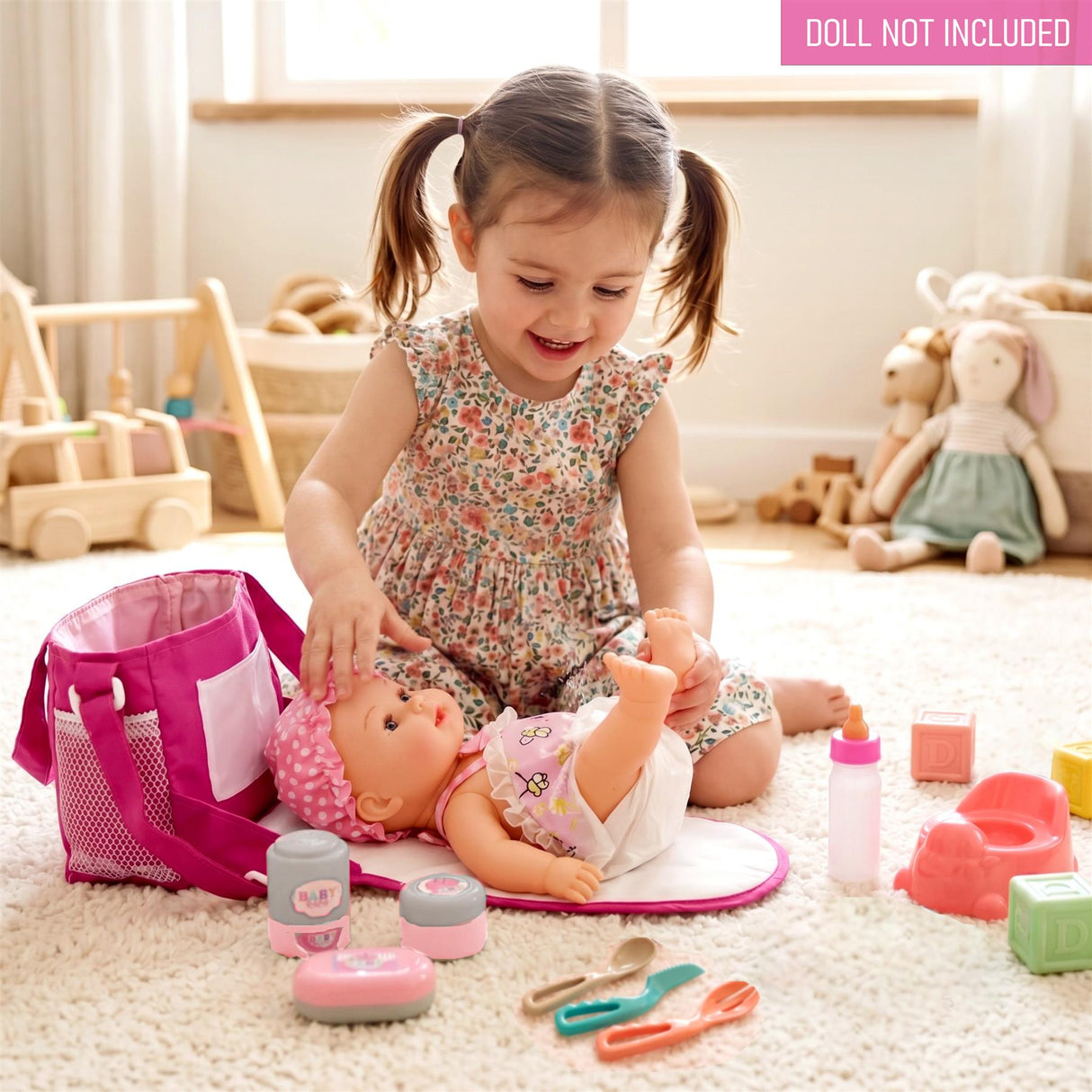 Pink changing bag, doll, and baby care accessories are arranged on a white surface.