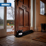 Fuzzy black cat draught excluder placed on the stone floor next to a wooden door.
